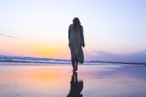 Aleksander Wiecki shares insights on the top IVF clinics for individuals over 50. The accompanying image features a woman strolling serenely along a sunlit beach.