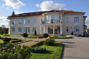 Modern, two-story Elite Clinic building with a landscaped garden and driveway, photographed on a sunny day.