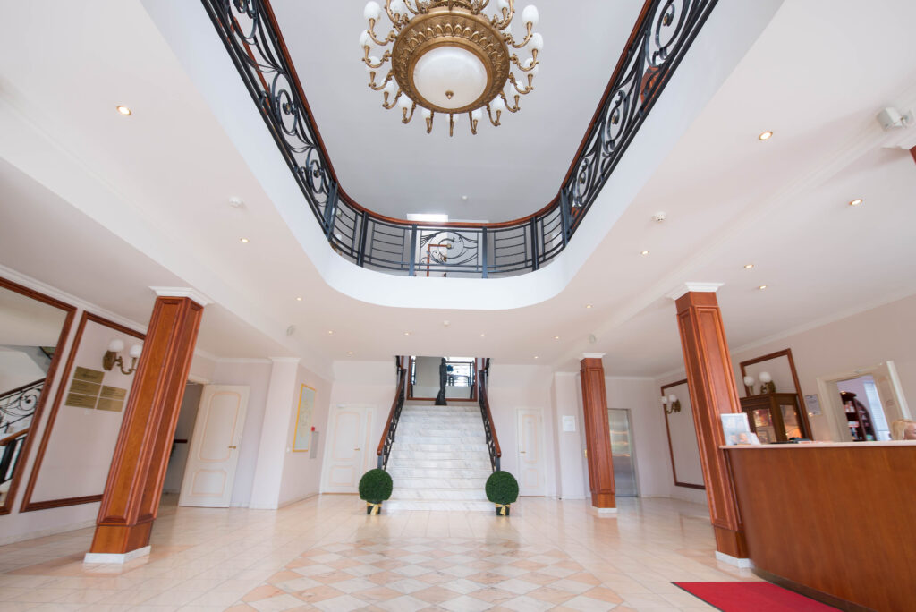 Elite Clinic Spacious and elegant clinic foyer featuring a grand staircase, chandelier, wood-paneled columns, and a modern reception desk.