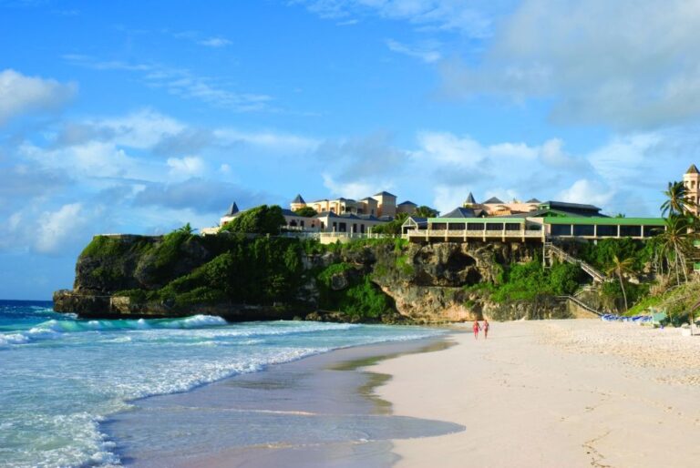 Crane Beach in Barbados featuring the iconic cliffside luxury resort, white sand, turquoise ocean, and palm trees on a bright sunny day
