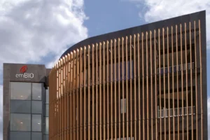Modern medical building. A sign on the left side reads “emBIO medical center,” and the building is set against a partly cloudy sky.