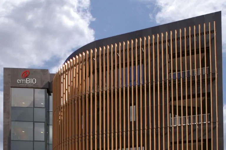 Modern medical building. A sign on the left side reads “emBIO medical center,” and the building is set against a partly cloudy sky.