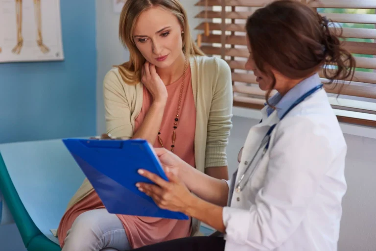 A woman sitting with a female doctor who is showing her information on a clipboard during a consultation.